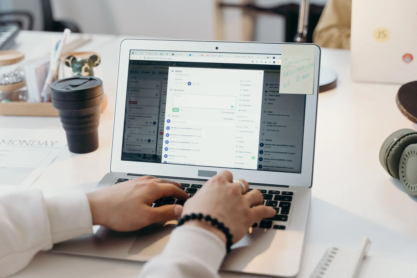 Hands typing on a laptop open on a list of tasks, beside a reusable coffee cup on a white desk